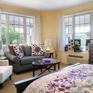 A cozy bedroom with a sitting area featuring a sofa, armchair, and coffee table, complemented by large windows and decorative elements.