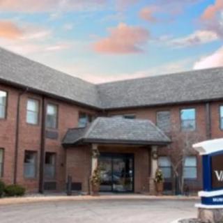 A brick building with a welcoming entrance and a sign outside, set against a colorful sky.