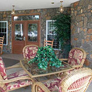 A cozy porch area featuring comfortable seating and a decorative glass table, surrounded by a stone wall.