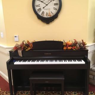 A digital piano adorned with autumn leaves sits beneath a wall clock.