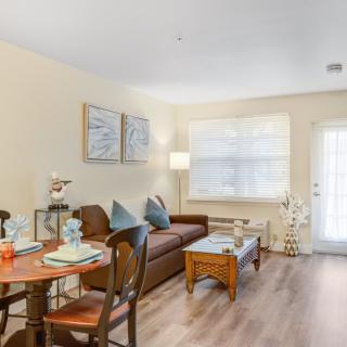 A cozy living room with a sofa, dining table, chairs, and a standing lamp near a window.