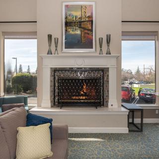 A cozy living room featuring a fireplace with a decorative mantel and artwork above, flanked by two large windows.