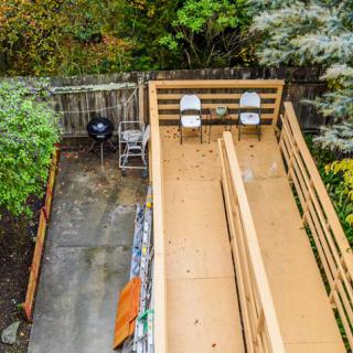 A wooden deck with seating and a grill, surrounded by lush greenery.