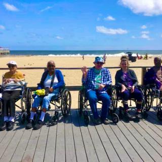 A group of elderly individuals in wheelchairs enjoying a sunny day at the beach.