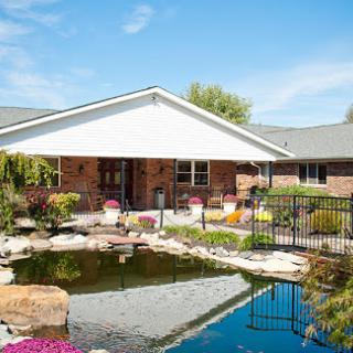 A beautiful house with a tranquil garden and pond under a clear blue sky.