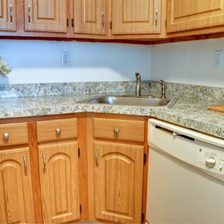 A kitchen with wooden cabinets and a granite countertop, featuring a sink and dishwasher.
