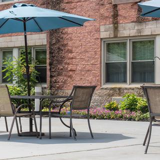 A sunny outdoor patio with a table and chairs under an umbrella, set against a brick building.