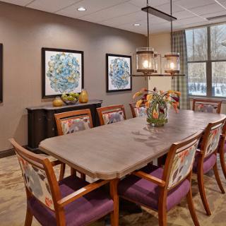 A modern dining room featuring a long wooden table, colorful chairs, and elegant lighting.