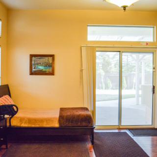 A cozy living room interior featuring a daybed next to a sliding glass door and window, with a painting on the wall and a carpet on the floor.