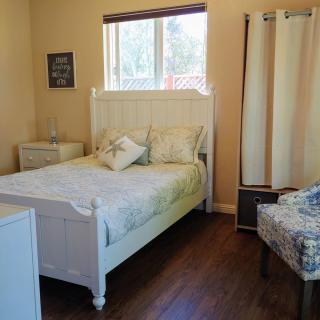 A cozy bedroom with a white bed, chair, and window letting in natural light.