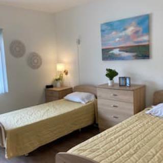 A cozy bedroom with two twin beds adorned with yellow bedspreads, featuring a dresser and a lamp, complemented by wall art and decor.