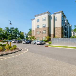 A modern apartment building with a parking lot and trees on a sunny day.