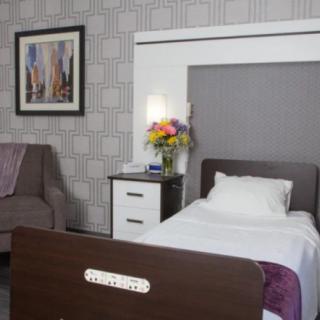 A cozy bedroom featuring a single bed, bedside table with flowers, and wall art.