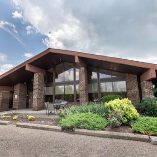 A modern building featuring large windows and a welcoming entrance surrounded by greenery.