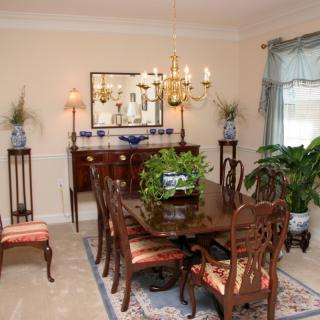 A traditional dining room with elegant furniture, a chandelier, and decorative elements such as plants and artwork.