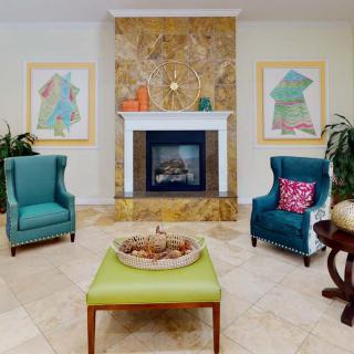 A cozy living room featuring a central fireplace with two chairs, vibrant artwork, and stylish decor.
