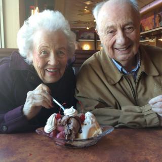 An elderly couple enjoying a dessert together in a restaurant.