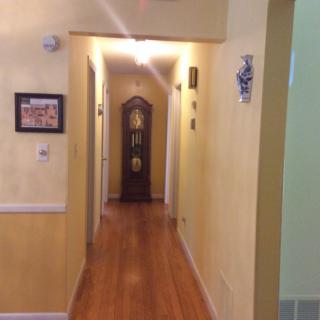 A hallway with wooden flooring, featuring a grandfather clock at the end and decorated with wall art.