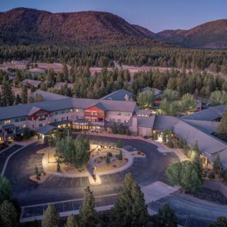 Aerial view of a building complex surrounded by forest and mountains at dusk.