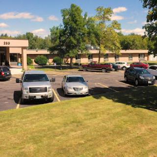 A view of a parking lot with various cars and a landscaped area featuring trees.