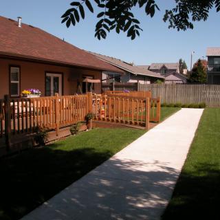 A backyard with a wooden fence and a concrete sidewalk leading to a house.