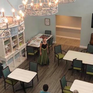 A dining area setup for an event with a person dressed in costume and elegant chandeliers overhead.