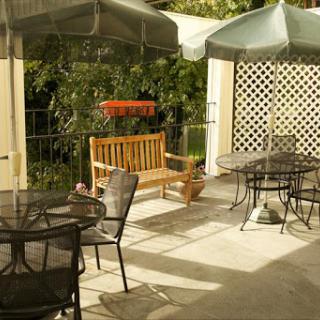 A cozy outdoor patio area featuring tables, chairs, and a wooden bench under sunshades.