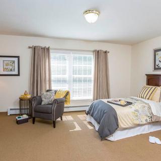 A well-lit bedroom with a cozy armchair and bed, featuring neutral decor.