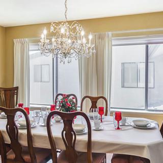 An elegantly set dining room table with a chandelier overhead and large windows providing natural light.