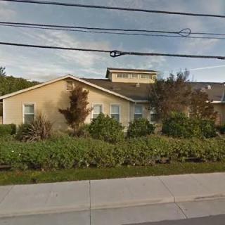 A suburban residential house with surrounding vegetation and a sidewalk in front.