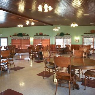 An empty dining hall with wooden chairs and tables arranged neatly under warm lighting.