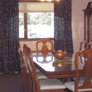 A classic dining room with a wooden table and chairs, complemented by dark curtains and a window view.