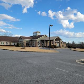 A modern building set against a partly cloudy sky, with an empty parking lot in the foreground.