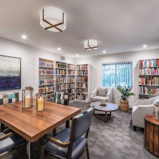 A cozy library room with bookshelves, a wooden table, and comfortable seating.