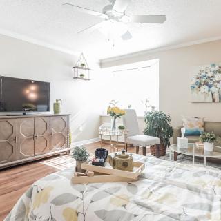 A modern and spacious bedroom with pastel colors, featuring a stylish TV stand, abundant natural light, and lush plants.