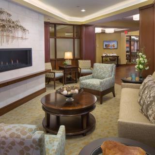 A cozy and elegantly decorated lobby with comfortable seating, including sofas and armchairs, centered around a wooden coffee table, complemented by decorative artwork on the walls.