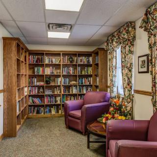 A cozy library corner with bookshelves, armchairs, and a small table with flowers.