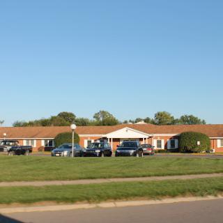 A view of a single-story residential building surrounded by vehicles and green grass under a clear blue sky.