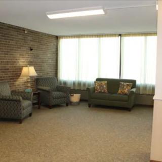 A cozy living room featuring a sofa, armchair, and lamp against a brick wall.