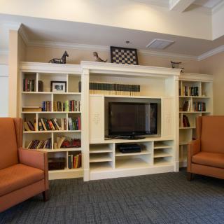 A cozy living room with a bookshelf, television, and comfortable chairs.
