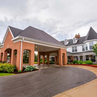 A residential building with a covered driveway and landscaped surroundings under a cloudy sky.