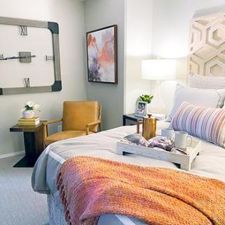 A cozy and modern bedroom with stylish decor, featuring a comfortable bed adorned with a throw blanket and decorative pillows, an armchair, side table, contemporary artwork, and soft lighting.