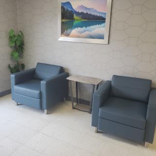 A cozy waiting area featuring two blue chairs, a small table, and decorative artwork on the wall.