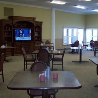 An empty dining area with tables and chairs, featuring a television mounted on a wooden cabinet.