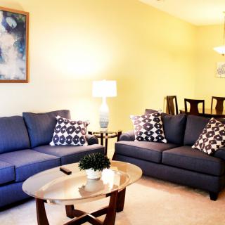 A cozy living room with blue sofas and a wooden coffee table, featuring stylish decor and artwork on the wall.