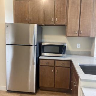 A modern kitchen corner with a stainless steel refrigerator, microwave, and wooden cabinets.