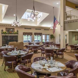 A dining room with neatly set tables and chairs, featuring chandeliers and an American flag.
