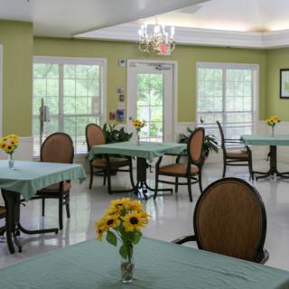A bright and inviting dining area featuring tables set with flower arrangements, surrounded by large windows.