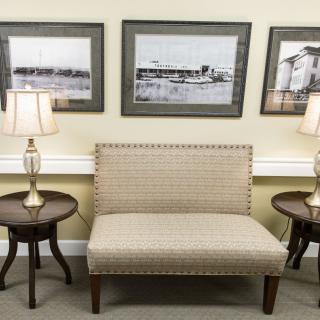 A cozy seating area with a sofa, side tables, and lamps against a backdrop of framed artwork.