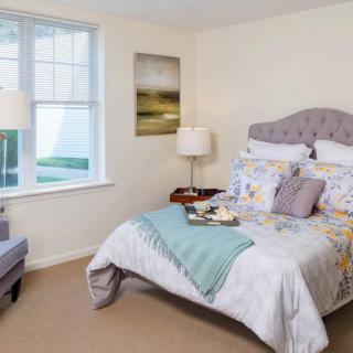 A cozy and well-decorated bedroom with a plush bed, soft lighting, and a large window.